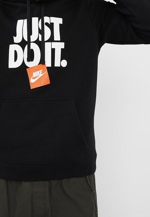 Sweat à capuche noir avec un large texte blanc "JUST DO IT." et une étiquette orange Nike suspendue aux cordons noirs.