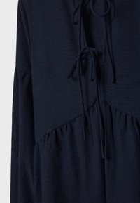 Vestido texturizado azul marino con una cintura fruncida, que presenta un detalle de lazo en el escote y un panel inferior fluido.