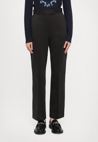 Čierne nohavice s rovnými nohavicami, so zväzkami a pruhmi; oblečené s čiernymi mokasínami a námorníckym sveterom.