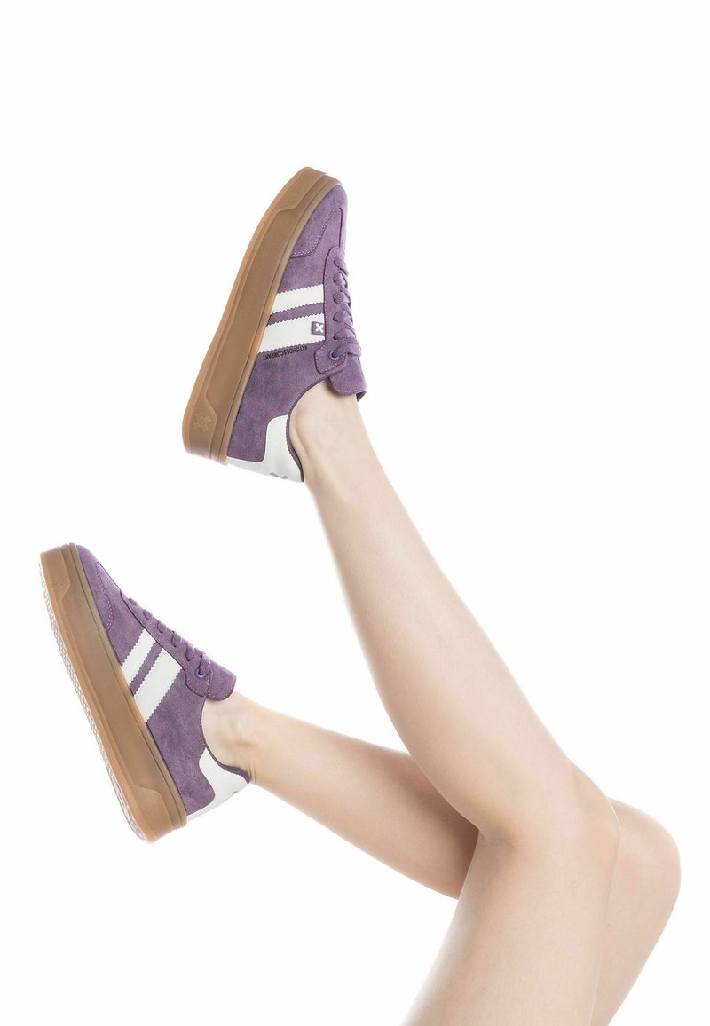Zapatillas de ante morado con rayas blancas y suela de goma, con cierre de cordones y un acento en el talón de contraste.