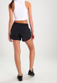 Pantalones cortos deportivos negros hechos de material ligero, con un ajuste relajado y dobladillo curvado. Se llevan con una camiseta blanca sin mangas.