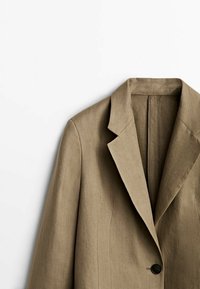 Savet khaki od lanenog materijala sa izrezanom reverom, zatvaranjem na jedan dugme i detaljima od vertikalnih šavova. Glatka tekstura i kroj prilagođen figuri.