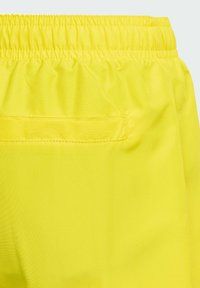 Šortky s elastickým pásom v jasne žltej farbe, vyrobené z hladkej tkaniny, s jednou zadnou vreckom so šitými detailmi.