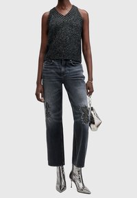 Svart glittrig stickad ärmlös topp, grå slitna jeans med pärlbroderade lappar och glänsande silverfärgade stilettklackade ankelstövlar. Mini metallisk väska.