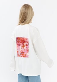 Biała bluza z długim rękawem i kwadratowym, kolorowym abstrakcyjnym wzorem w różowym, pomarańczowym i czerwonym na plecach. Luźny krój i materiał.