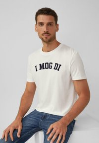Weißes Baumwoll-T-Shirt mit navyblauem gesticktem Text "I MOG DI", kurze Ärmel, runder Halsausschnitt, kombiniert mit dunkelblauen Jeans.