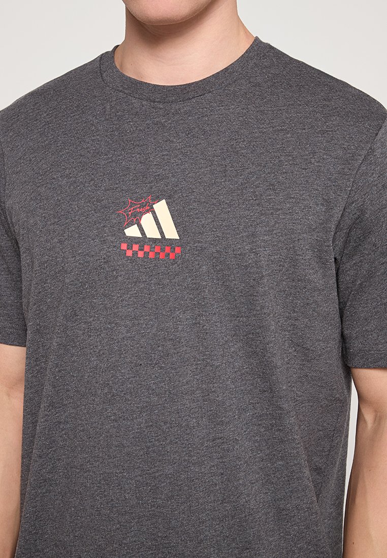 T-shirt in cotone grigio con un piccolo design grafico crema e rosso sul petto che ricorda un logo stilizzato adidas e un motivo a scacchi.