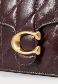 Burgundy leather bag with a quilted texture, featuring a prominent gold hardware clasp and contrasting black stitching details.
