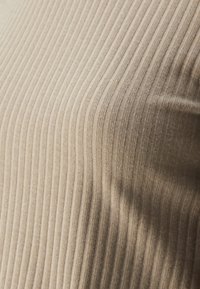 Pješčana rebrasta pletenina s vertikalnim linijama, meka tekstura, blago rastezljiva, reflektira svjetlost na određenim dijelovima. Pogodna za odjeću.