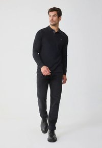 Zwart poloshirt met lange mouwen en een contrasterende kraag, gecombineerd met donkere spijkerbroek en zwarte schoenen. Minimalistisch ontwerp, gladde textuur.