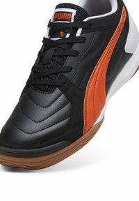Scarpa sportiva nera e arancione con pelle testurizzata, suola in gomma e il prominente logo Puma sulla linguetta. Presenta lacci e contorni lisci.
