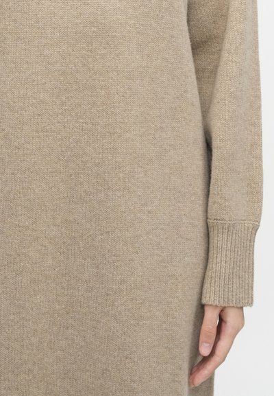 Bež pleteni džemper koji se udobno pristaje, s rebrastim manšetama i mekanom teksturiranom završnom obradom, produžen do sredine bedara za moderan siluetu.