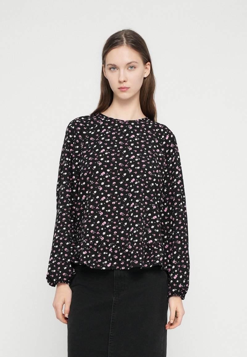 Top nero a maniche lunghe con scollo rotondo, caratterizzato da un motivo floreale in rosa e bianco e maniche arricciate. Abbinato a una gonna nera.