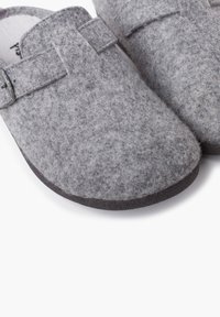 Scarpe slip-on grigie con una texture morbida, dotate di una suola piatta in gomma nera e un semplice dettaglio a strap sulla parte superiore.