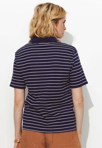 Polo shirt rayé bleu marine et blanc à manches courtes et col, avec une coupe décontractée et une texture côtelée, associé à un short marron rayé.