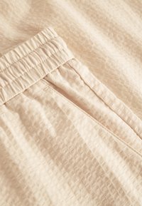 Hele bee ž tekstuuriga kangas peene ruudumustriga, millel on elastne vöökoht ja küljetasku detail.