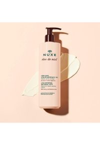 NUXE Rêve de Miel bodycrème in een lichtroze fles met een zwarte pomp. De tekst vermeldt ultra verzachtend, 48 uur hydratatie en natuurlijke ingrediënten.
