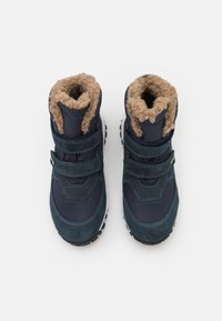 Marineblaue Winterstiefel mit einem weichen, beigen Fellfutter am Kragen, ausgestattet mit Klettverschlüssen und einer robusten schwarzen Sohle für besseren Halt.