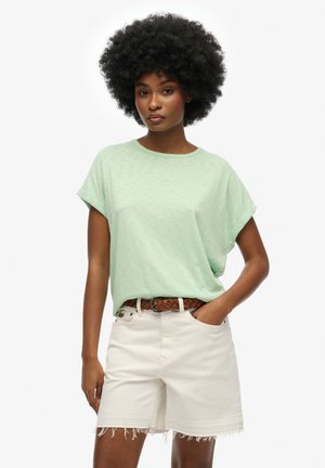 Mintgrøn kortærmet t-shirt med rund halsudskæring, parret med lysebeige shorts med frynsekanter og et brunt vævet bælte.