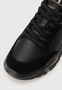 Svart sneakers med en kombinasjon av glatt skinn og teksturert semsket skinn, med runde lissser og en mønstret såle. Sølvfargede detaljer er synlige.