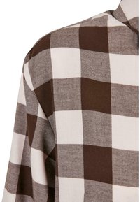 Tissu à carreaux brun et blanc avec un grand motif carré, montrant la zone de l'épaule et du col d'un vêtement.