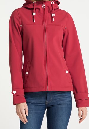 Chaqueta roja con capucha, cremallera frontal, cordones ajustables, bolsillos con botones a presión y correas en los puños, usada con vaqueros azules.