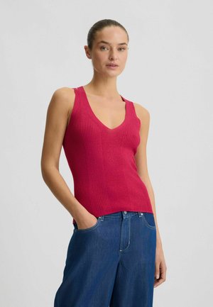 Figurbetontes, geripptes Tanktop in lebhaftem Pink mit V-Ausschnitt und breiten Schulterträgern, kombiniert mit lockeren blauen Jeans.