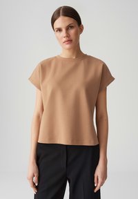 Top beige in cotone misto a maniche corte con scollatura rotonda, vestibilità comoda e texture liscia, abbinato a pantaloni neri.