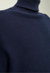 Primo piano di un maglione a collo alto a coste blu navy con tessuto a maglia testurizzato sulla parte superiore del torso.