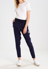 Marina atletiska joggers med vita accentstreck, elastisk midja med dragsko och sidofickor. Kombination med en vit t-shirt med kort ärm.