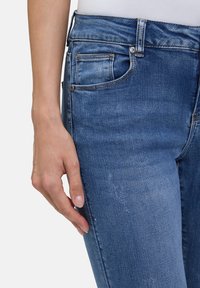 Jeans en denim bleu moyen avec une texture lisse, dotés de cinq poches, de légères décolorations et d'une taille standard.