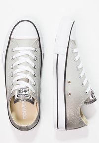 Silver canvas sneakers with white laces, glittery texture, rubber toe cap, and black accents on the sole and logo.