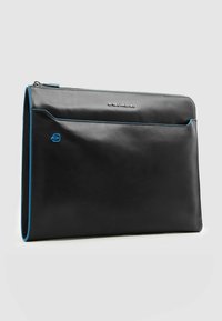 Funda para portátil de cuero negro con costuras decorativas en azul, con cierre superior de cremallera y bolsillo frontal. Logotipo visible de forma destacada en el frente.