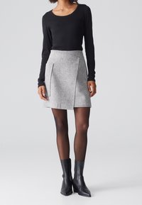 Falda gris texturizada con pliegues frontales, combinada con una blusa negra de manga larga y botas negras hasta el tobillo, creando un conjunto coordinado.