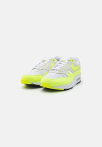 Adidași albi și galbeni neon, cu un superior din plasă și piele întoarsă, vârful rotund, guler căptușit și amortizare vizibilă în talpă.