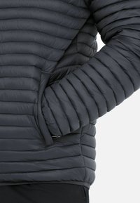 Veste rembourrée gris foncé avec des panneaux matelassés horizontaux, des poches latérales et une texture lisse. Design léger et ajusté.