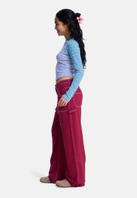 Modrá a biela pruhovaná košeľa s dlhým rukávom, skrátený strih. Červené široké nohavice s kontrastným prešitím a bočnými vreckami. Neformálna obuv.