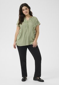 Chemise vert clair à manches courtes avec des rayures blanches verticales et un col en V, associée à un pantalon noir et des mocassins noirs brillants.