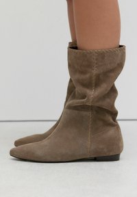 Brown suede ankle boots featuring a slouchy design, pointed toe, and visible stitching detail along the side. Flat sole for easy wear.