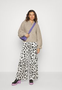 Beige gebreide vest met rits, wijde witte broek met zwart luipaardmotief en zwarte platform schoenen met paarse accenten. Paarse schoudertas.