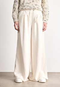 Pantaloni largi cu talie elastică și șnur, de culoare crem, dintr-un material moale, cu accente de cusături laterale.