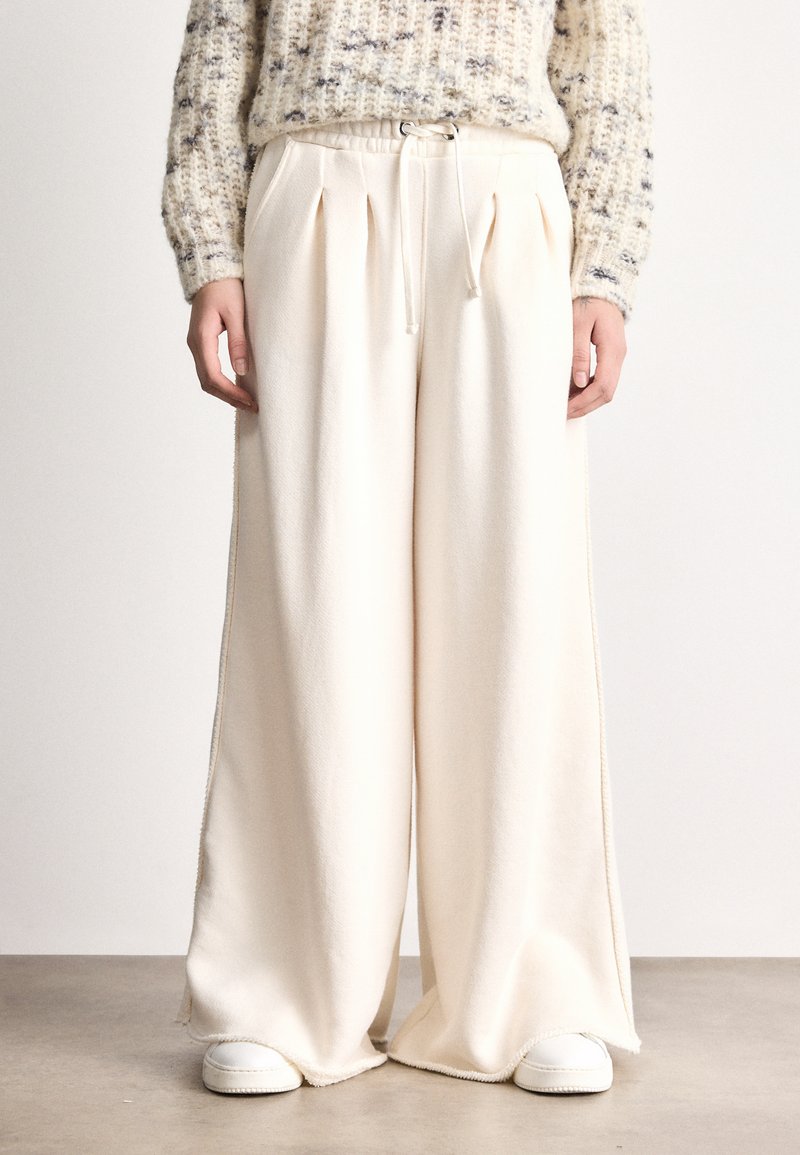 Pantaloni largi cu talie elastică și șnur, de culoare crem, dintr-un material moale, cu accente de cusături laterale.