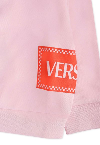 Felpa rosa chiaro con un vivace patch rettangolare rosso con la parola "VERS" in bianco, su un tessuto testurizzato.