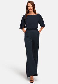Marine jumpsuit met een bateau-halslijn en brede, uitlopende pijpen. Gemaakt van een gladde stof. Heeft korte mouwen en zijzakken.