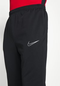 Pantalons de sport noirs avec une taille élastique et un logo Nike argenté sur la cuisse gauche, fabriqués dans un tissu lisse et léger.