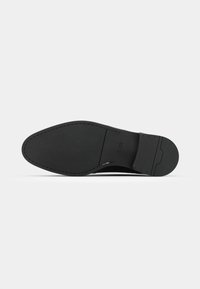 Black leather shoe with a smooth texture, pointed toe, and stitched detailing. The sole is flat with a slight heel and a branded accent.