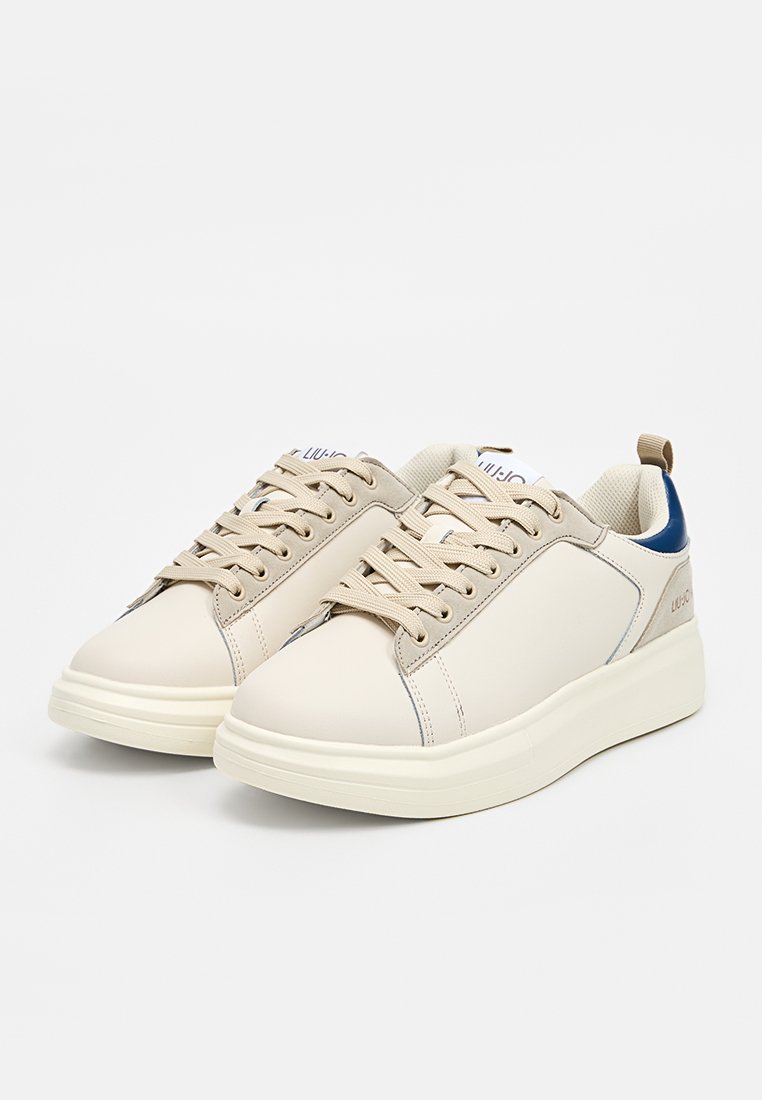 Sneakers beige realizzati in materiale sintetico liscio, con lacci testurizzati, collo imbottito e un accento di tacco navy a contrasto.
