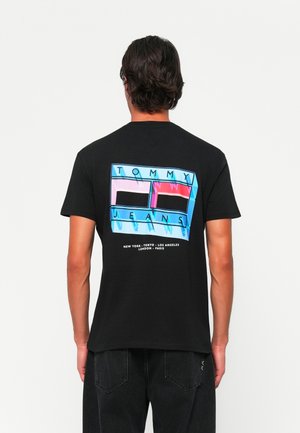 Black cotton T-shirt featuring a colorful graphic design on the back with "TOMMY" and "JEANS" text, alongside city names in white.