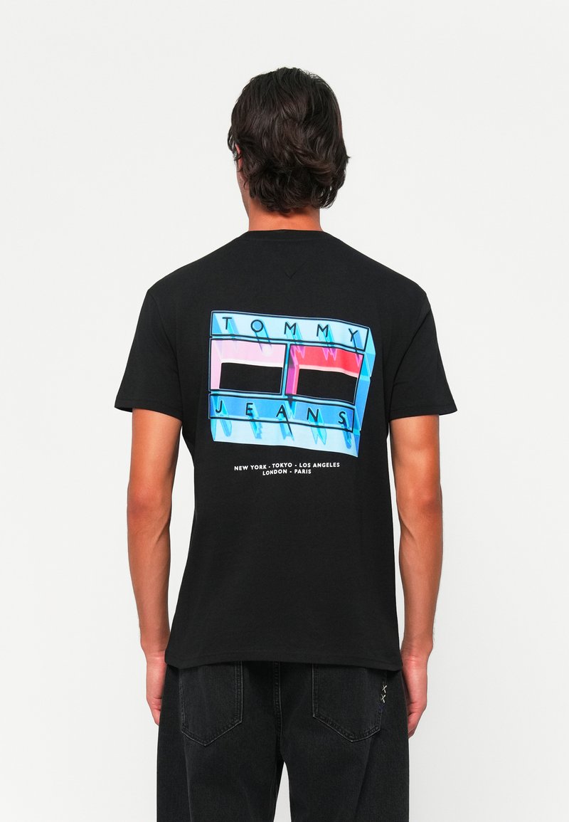 Schwarzes Baumwoll-T-Shirt mit einem bunten Grafikdesign auf der Rückseite, das den Text "TOMMY" und "JEANS" sowie Städtenamen in Weiß enthält.