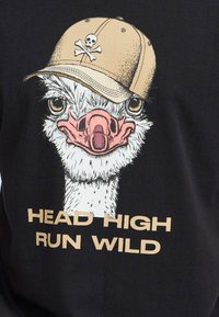 Sort t-shirt med en tegneserie-struisvogel iført en beige kasket med et dødningehoved og krydsede knogler. Teksten lyder "HEAD HIGH RUN WILD" i beige.